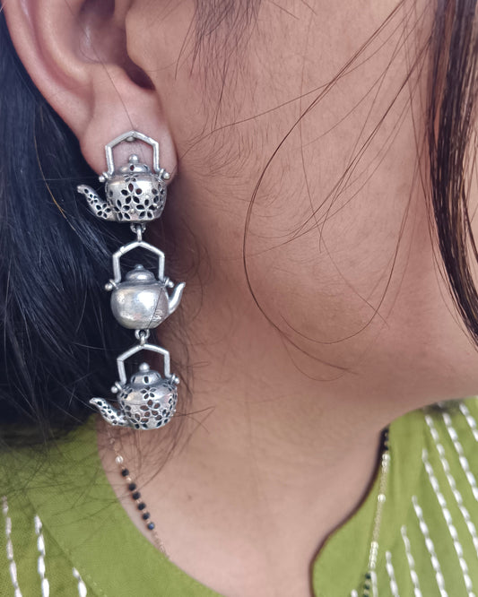 Close-up of a person wearing a decorative silver earring with a teapot design.