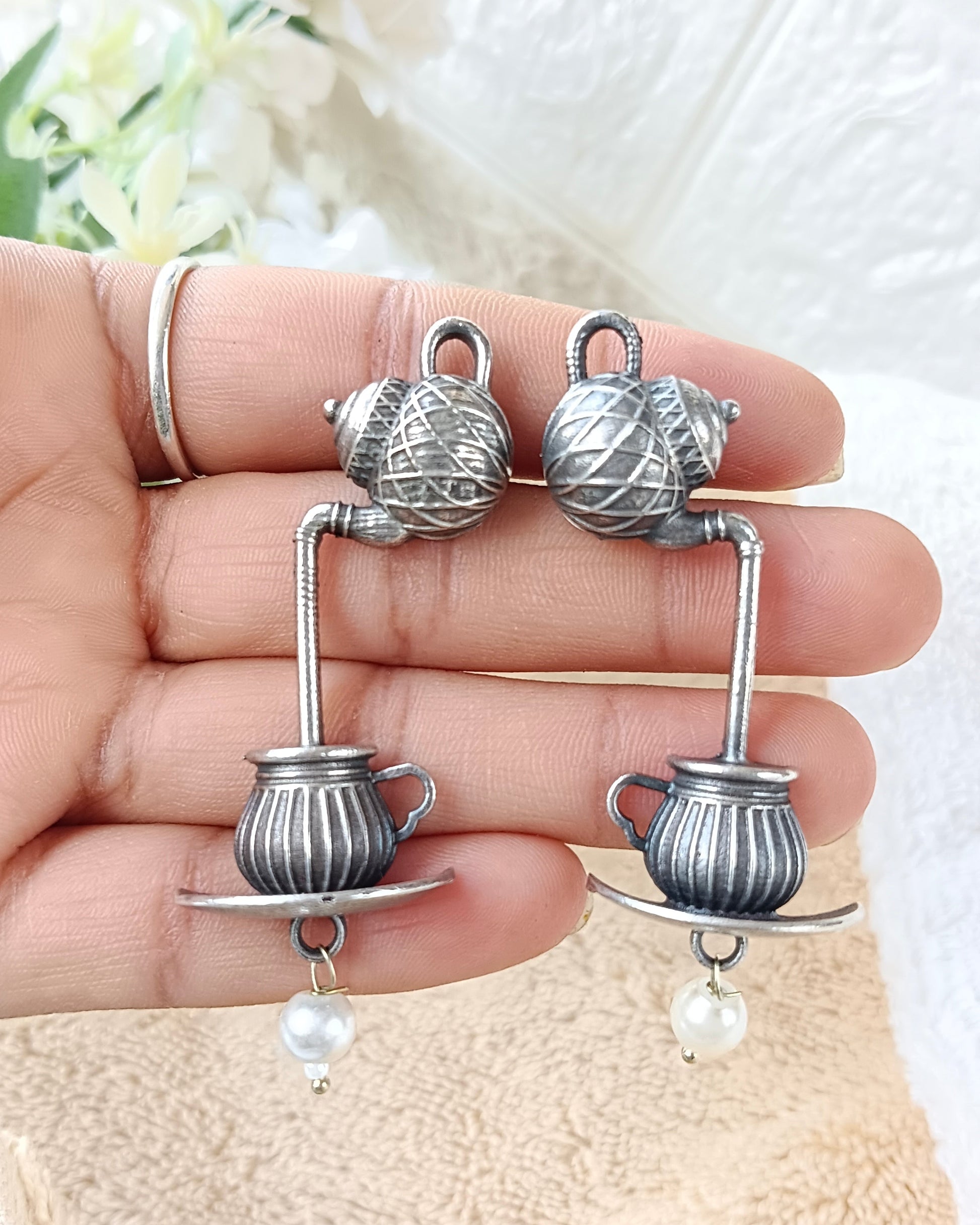 Silver earrings with pearl drops held in a hand against a textured white background.