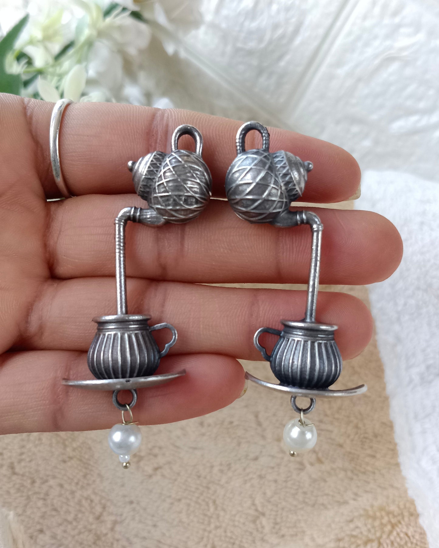 Silver teacup earrings with pearls held in a hand against a white background
