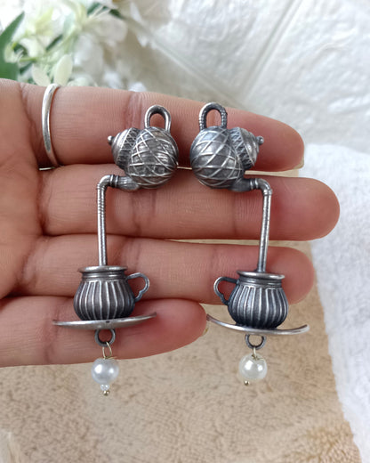 Silver teacup earrings with pearls held in a hand against a white background