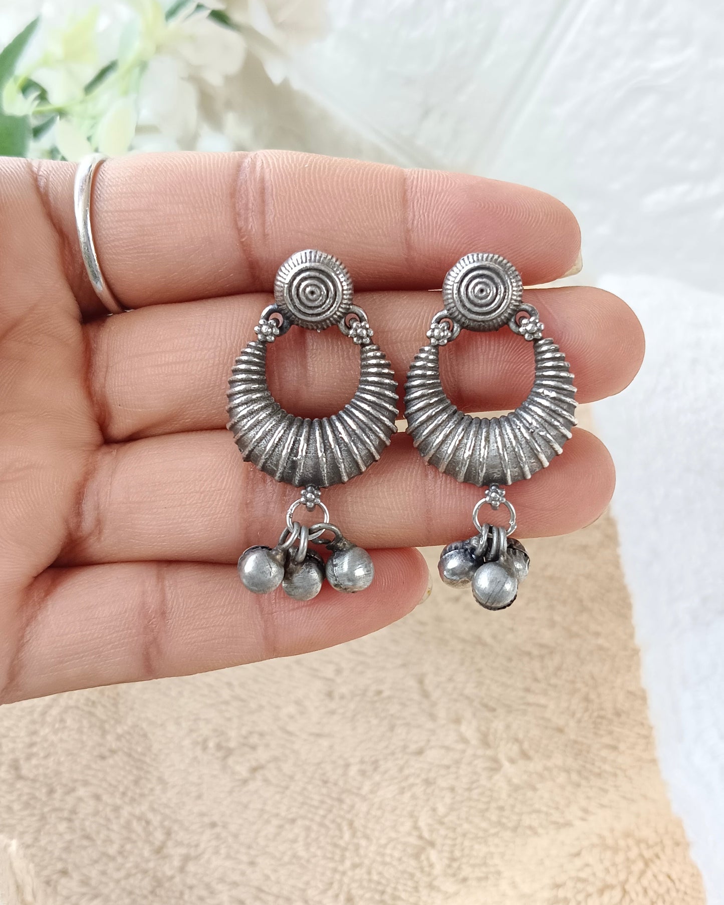 Silver earrings with circular designs and dangling beads held in a hand against a white background.