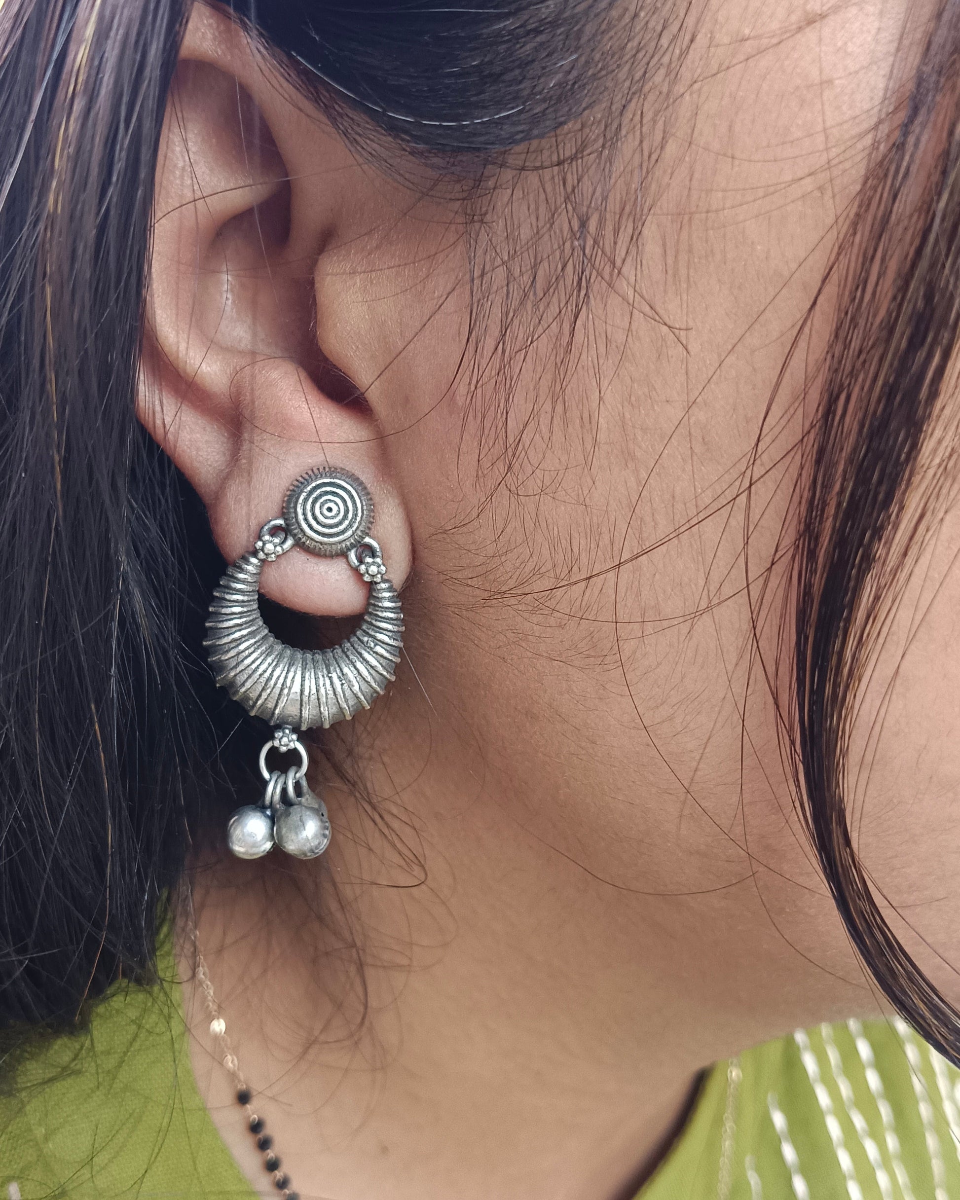 Close-up of an ear wearing a silver earring with circular design and dangling elements.