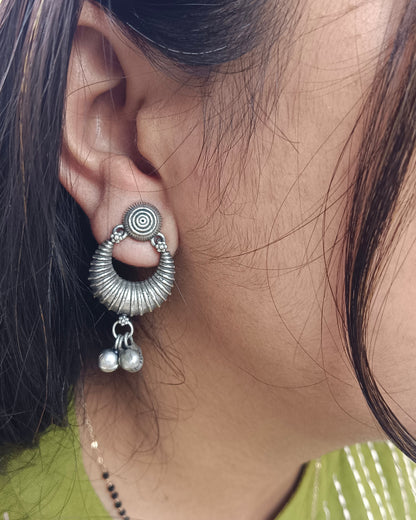 Close-up of an ear wearing a silver earring with circular design and dangling elements.