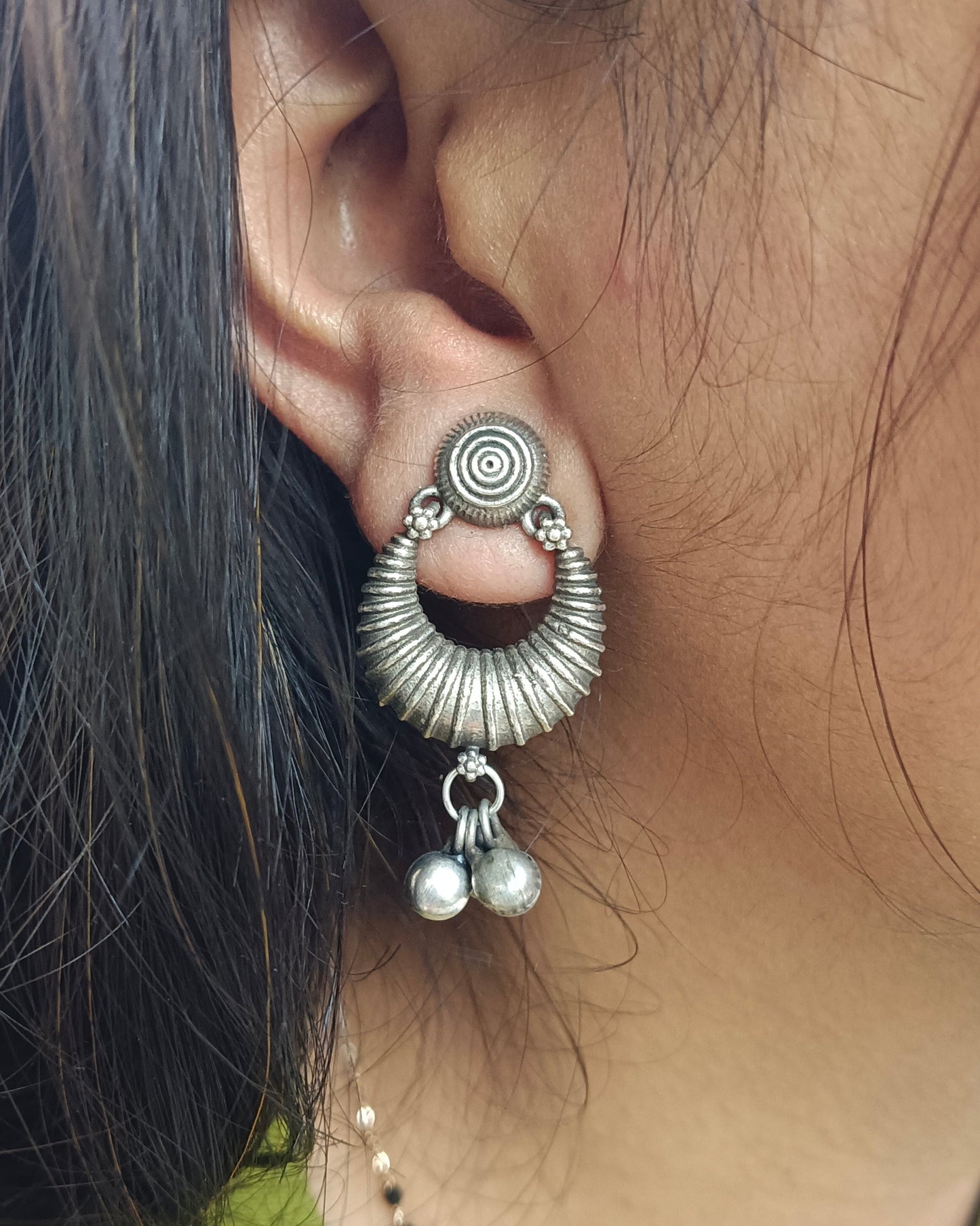Close-up of an ear wearing a silver earring with pearl-like beads.