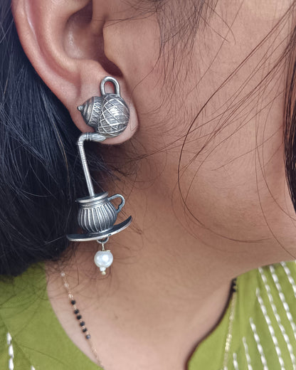 Close-up of a person wearing a silver earring with a pearl, against a blurred background.
