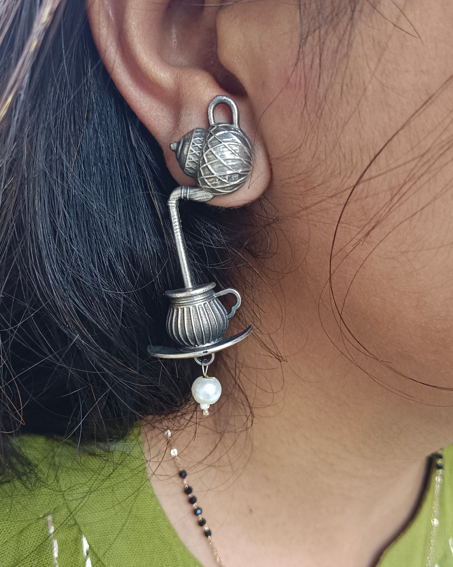 Close-up of an ear wearing a decorative silver earring with a pearl, against a blurred background.
