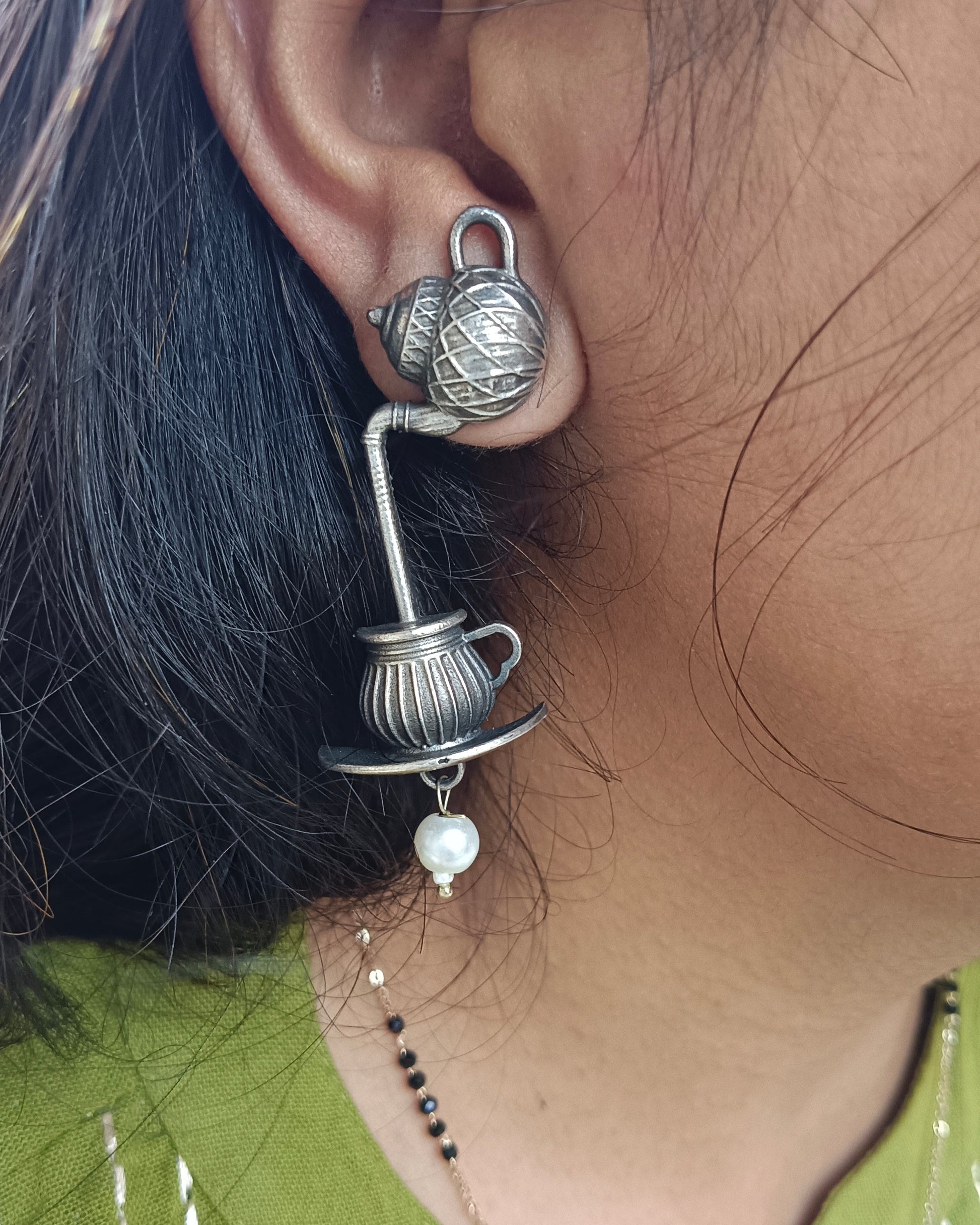 Close-up of an ear wearing a decorative silver earring with a pearl, against a blurred background.