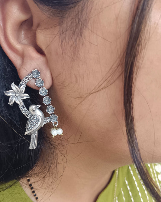 Close-up of a person wearing a silver earring with a bird design.