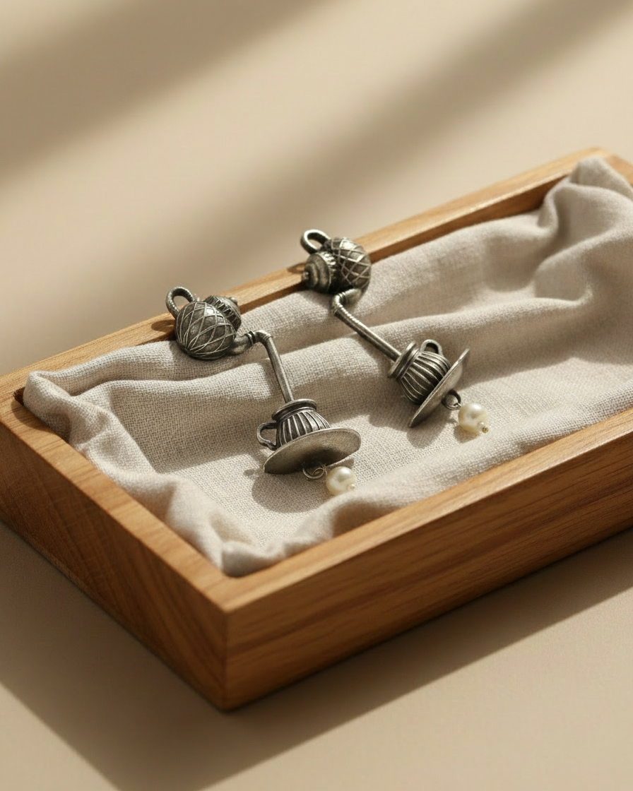 Pair of silver earrings with pearls in a wooden display box on a beige background
