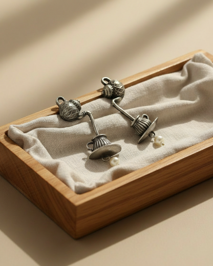 Pair of silver earrings with pearls in a wooden display box on a beige background