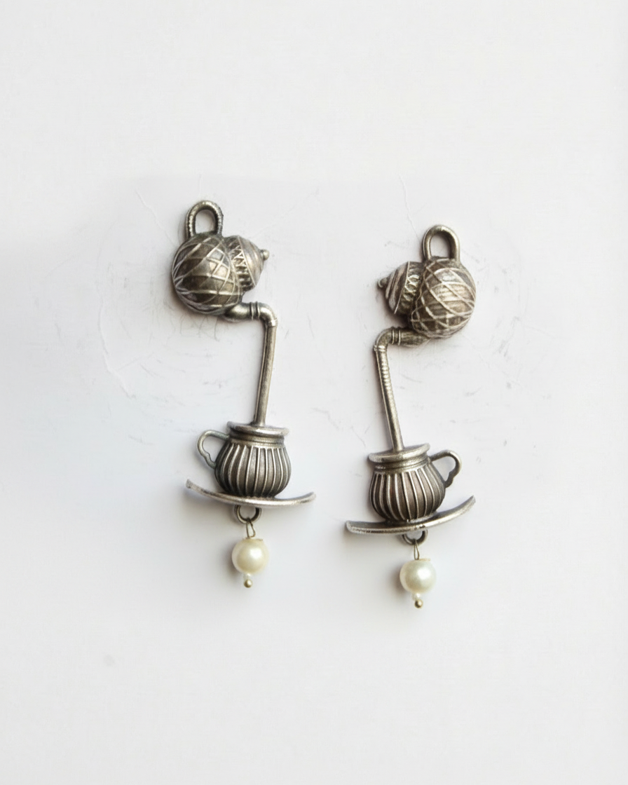 Pair of silver earrings with teacup and pearl design on a white background