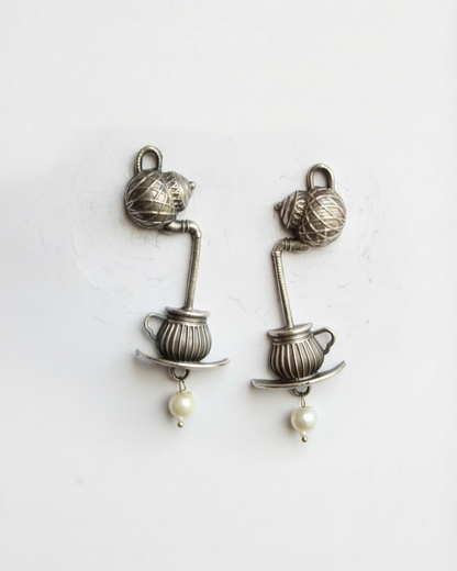 Pair of silver earrings with teacup and pearl design on a white background