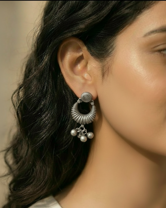 Close-up of a woman wearing a silver earring with black center and dangling beads.